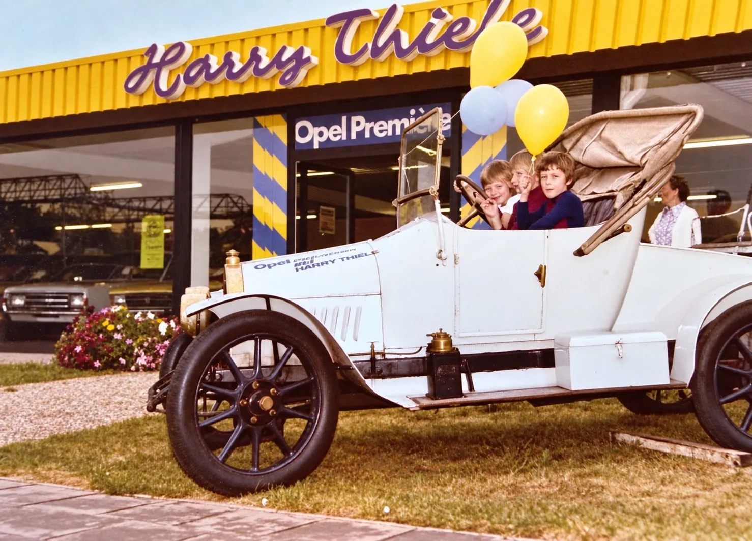 Historische Aufnahme: Autohaus Harry Thiele in Garbsen zur Opel-Premiere, davor ein Oldtimer mit Kindern und Luftballons