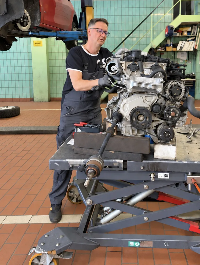 Kfz-Mechatroniker arbeitet in der Werkstatt an einem ausgebauten Motor